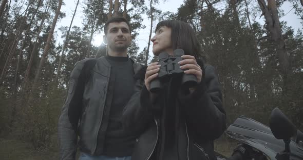 Bottom Angle View of Couple of Happy Interracial Bikers Standing Outdoors with Binoculars. Smiling alt