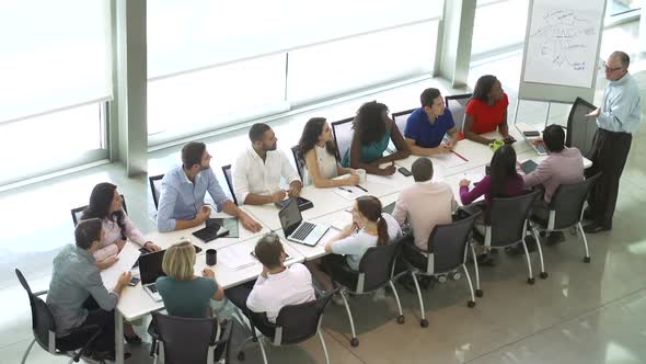 Businessman Addressing Meeting Around Boardroom Table alt