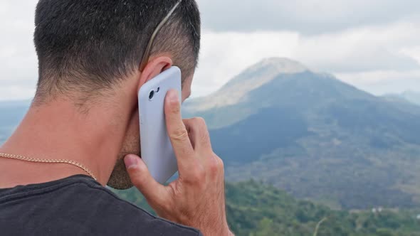 A Brunette with Sparse Gray Hair Holds Phone to His Ear and Talks Looking at a Majestic Volcano