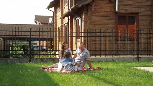 Happy Young Woman and Man Sit with Little Boy on Lawn alt