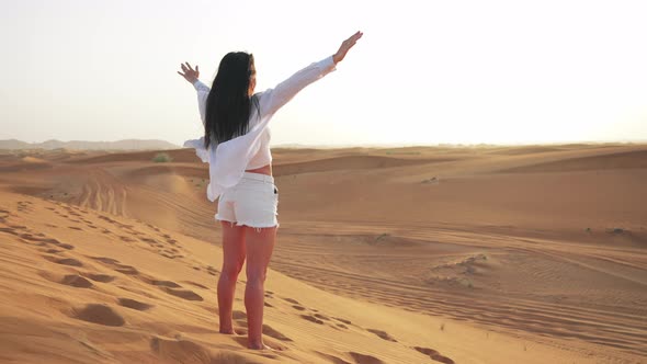 Back View Young Beautiful Caucasian Woman Standing in Sandy Desert and Raises Her Hands Up alt