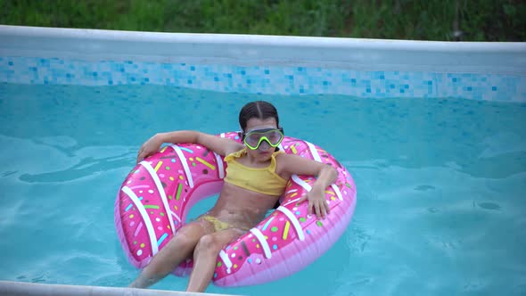 Girl Plays an Inflatable Ring is in Swimming Pool in the Garden