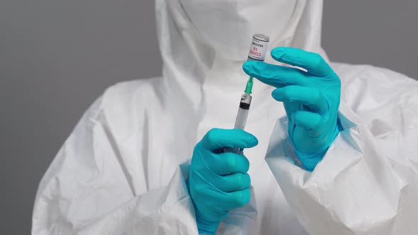 doctor in protective PPE suit drawing Coronavirus (Covid-19) vaccine bottle into syringe injection