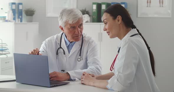 Team of Doctors Working Together in Hospital Checking Patient Test Results on Laptop alt