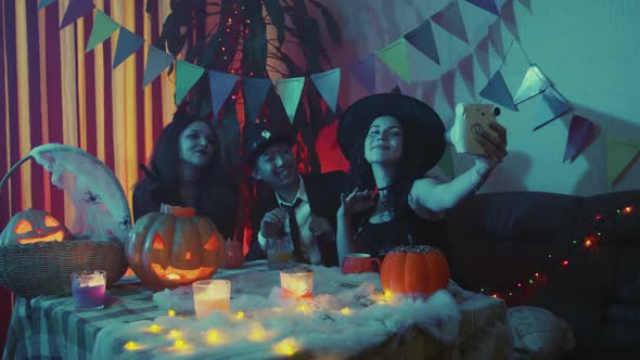 A Group of Friends are Sitting at a Table in Creepy Costumes Taking Pictures with a Camera and alt