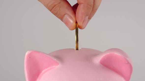Male hand throws golden coin into a pink piggy moneybox
