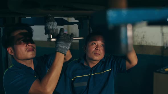 Skillful Asian guy in uniform fixing car at mechanics garage at night.