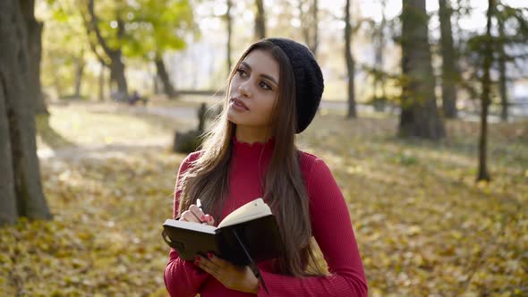 Young Poetess Inspects the Autumn Park and Writes Down Her Thoughts in Notebook alt