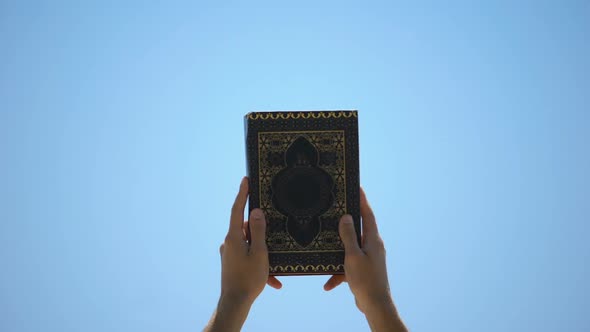 Male Hands Raising Koran to Sky, Sharing Sacramental Islamic Teachings, Faith alt
