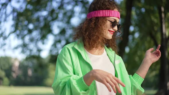 Joyful Relaxed Caucasian Woman in Retro Outfit and Sunglasses Dancing in Slow Motion Outdoors in alt