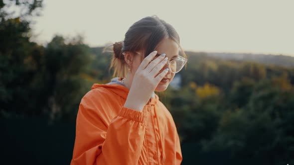 The Optimistic Young Woman with Her Hair in a Bun Arranges Her Glasses and Displays a Wide Smile on alt