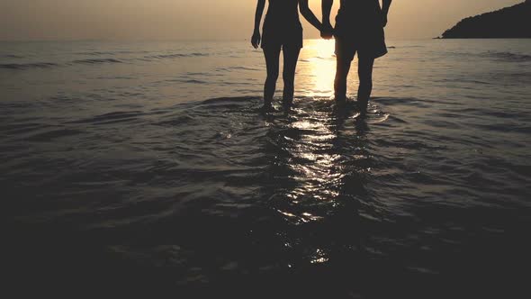 Silhouette of romantic couple lover holding hands while walking at the beach in sunset
