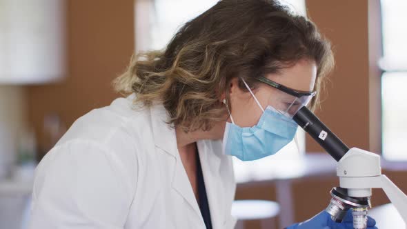 Female teacher wearing face mask and protective glasses using microscope in laboratory alt