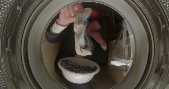 A Man Holds a Dirty Sock in His Hands in the Washing Machine alt