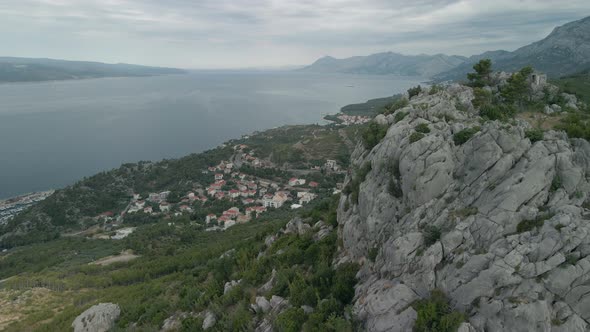 Drone Flying Past a Large Rock Against the Backdrop of a Small Town on the Coast of Croatia