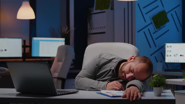 Exhausted Overworked Businessman Sleeping on Desk Table in Startup Business Office alt