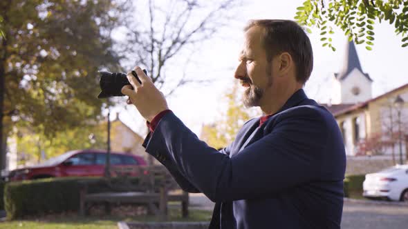 A Middleaged Handsome Caucasian Man Takes Pictures with a Camera As He Sits on a Bench