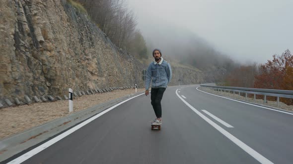 Young Man with a Beard Riding Skateboard Cruising Downhill on Countryside Road