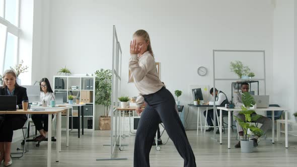 Beautiful Young Blonde Dancing in Office While Colleagues Clapping Hands in Background alt
