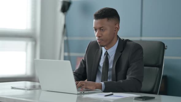 African Businessman Pointing at Camera while using Laptop in Office alt