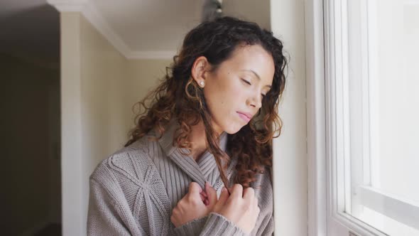 Thoughtful biracial woman standing at window and looking into distance alt