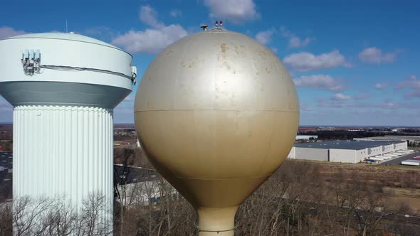 An aerial shot orbiting a silver water tower with another blue one in the background. The drone came alt