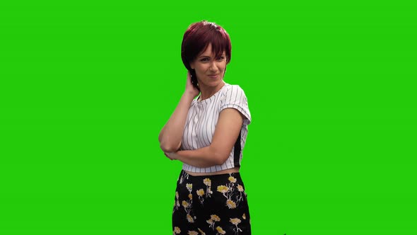 Cheerful short haired brunette female adjusting hair on green screen alt