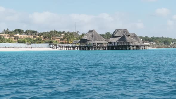 African Restaurant with Thatched Roof on Wooden Poles Above the Ocean alt