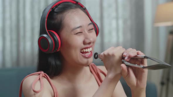 Smiling Asian Woman Listening To Music With Headphones And Singing While Slicing The Cucumber alt