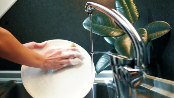 Girl washing white plate in modern kitchen with dark scandinavian design