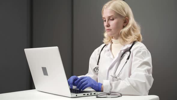 Woman Doctor Working at Computer Entering Data From Patient File alt