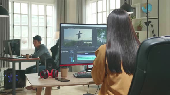 Back View Of Asian Female Video Editor Works With Footage And Sound On Computer In Office alt