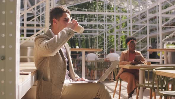  Businessman Drinking Coffee and Working on Laptop in Cafe alt