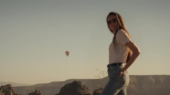 Woman in Glasses Standing Against Hot Air Balloon Flying Above Valley