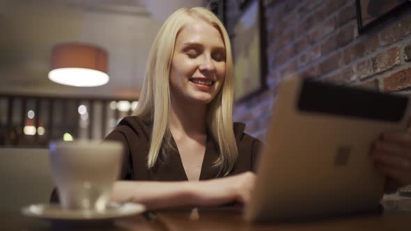Young Attractive Woman is Talking on Video Call Using Tablet in a Restaurant alt