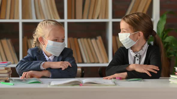Young schoolgirls in protective medical masks sitting at table desk in the classroom