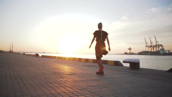 Young Stylish Funky Girl with Green Hair Riding Roller Skates and Dancing Near Sea Port During alt
