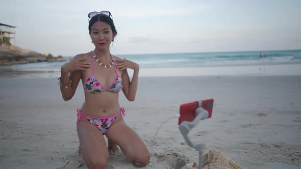 Asian Thai Girl in Bikini Swimwear on a Beach Shooting TikTok Video at Sunset alt