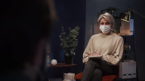 Psychologist Therapy Session Woman and Man Wearing Face Mask Sitting on the Sofa and Talking alt