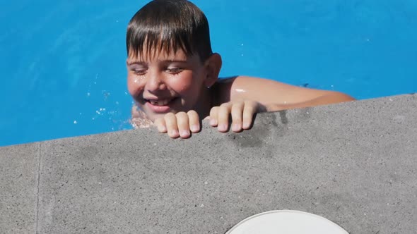 A Cheerful Teenage Boy Bathes in the Pool Moving Along the Edge of the Pool Holding and Moving His alt