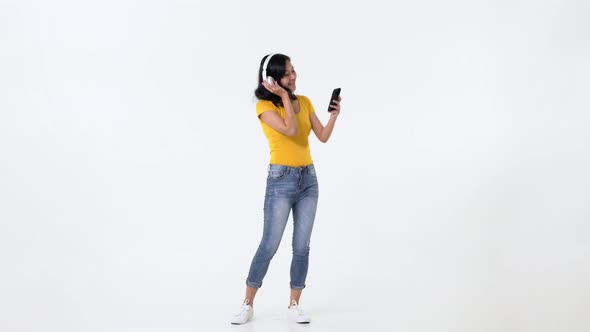 Smiling beautiful young asian woman holding mobile phone in hand enjoying the music