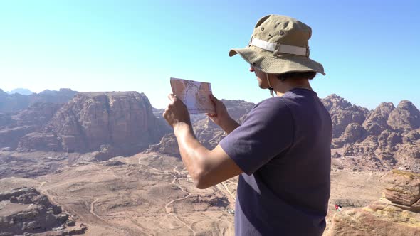 Man with map standing at the edge of mountains and looking around navigation