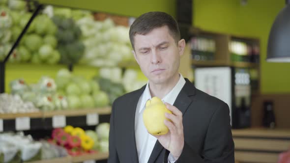Young Caucasian Man Looking at Yellow Pear in Grocery and Showing Thumb Up. Confident Guy Choosing alt