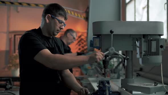 Workers stand behind drilling machines and make holes in parts in a furniture factory.