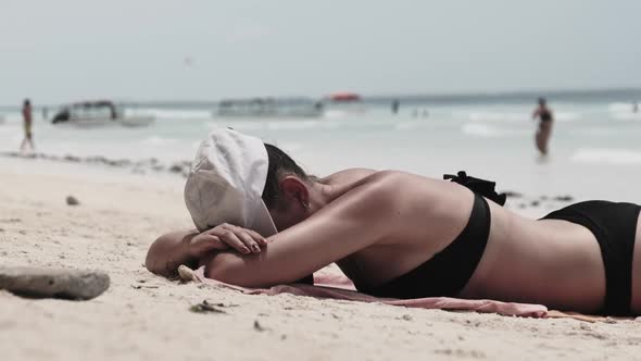 Young Woman Sunbathes on a Paradise Sandy Beach Lying in Black Bikini Near Ocean alt