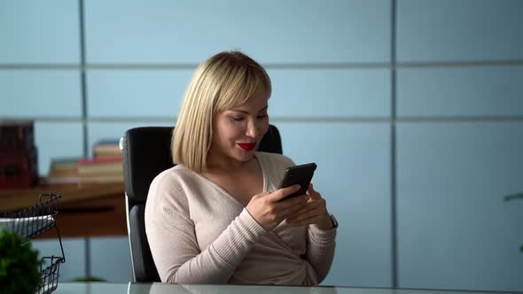 Businesswoman Is Relaxing in Her Office Room, Swaying in Chair and Surfing Internet By Smartphone alt