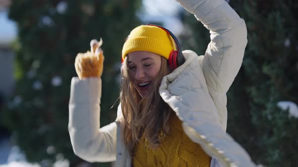 Happy Young Woman Dancing to Music in Headphones Singing on Cold Winter Sunny Day Outdoors alt