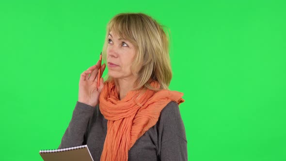 Portrait of Middle Aged Blonde Woman Is Thinking, Then Writing with Pencil in Notebook. Green Screen alt