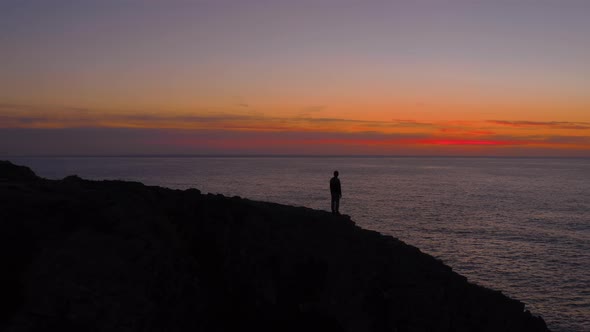 Silhouette of Man Walk on Edge of Cliff at Sunset