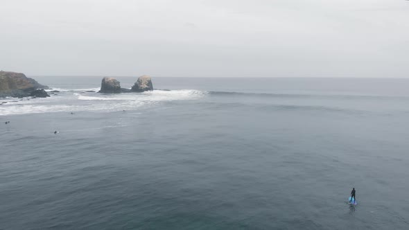 Aerial reveal of person paddle on a cloudy day at the Sea, Pichilemu, Chile-4K alt
